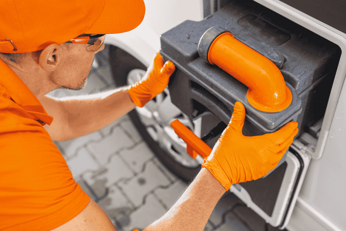 Person in orange gloves handling an RV sewage hose connection at a vehicle waste disposal point during a Chili Cook-Off.