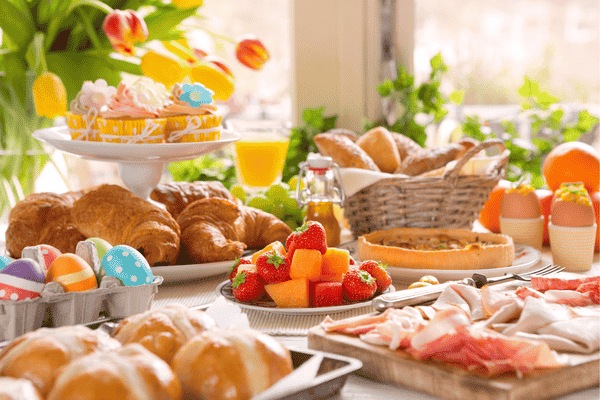 Easter Brunch spread with pastries, fruit, decorated eggs, bread, cold cuts, and spring flowers arranged for a festive celebration.