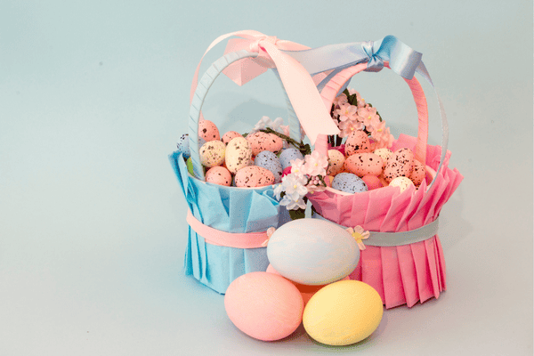 Two pastel baskets with Easter eggs and flowers, one blue, one pink, with decorated eggs in front—a charming Easter craft display.