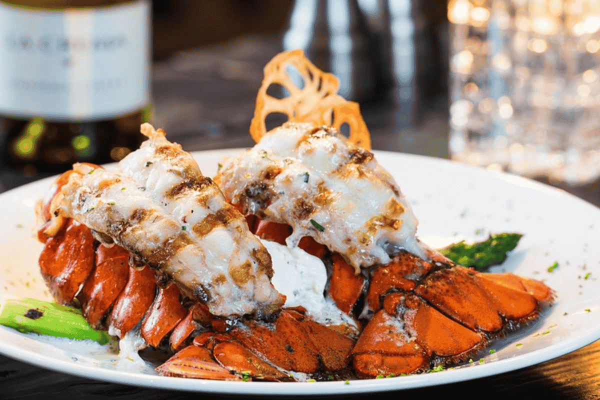 Grilled lobster tails served on a white plate with sauce and garnished with vegetables, a signature dish at Workshop Kitchen.