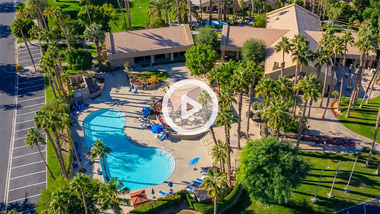 Aerial view of Emerald Desert RV Resort with a large outdoor pool, lounge chairs, palm trees, and surrounding buildings.