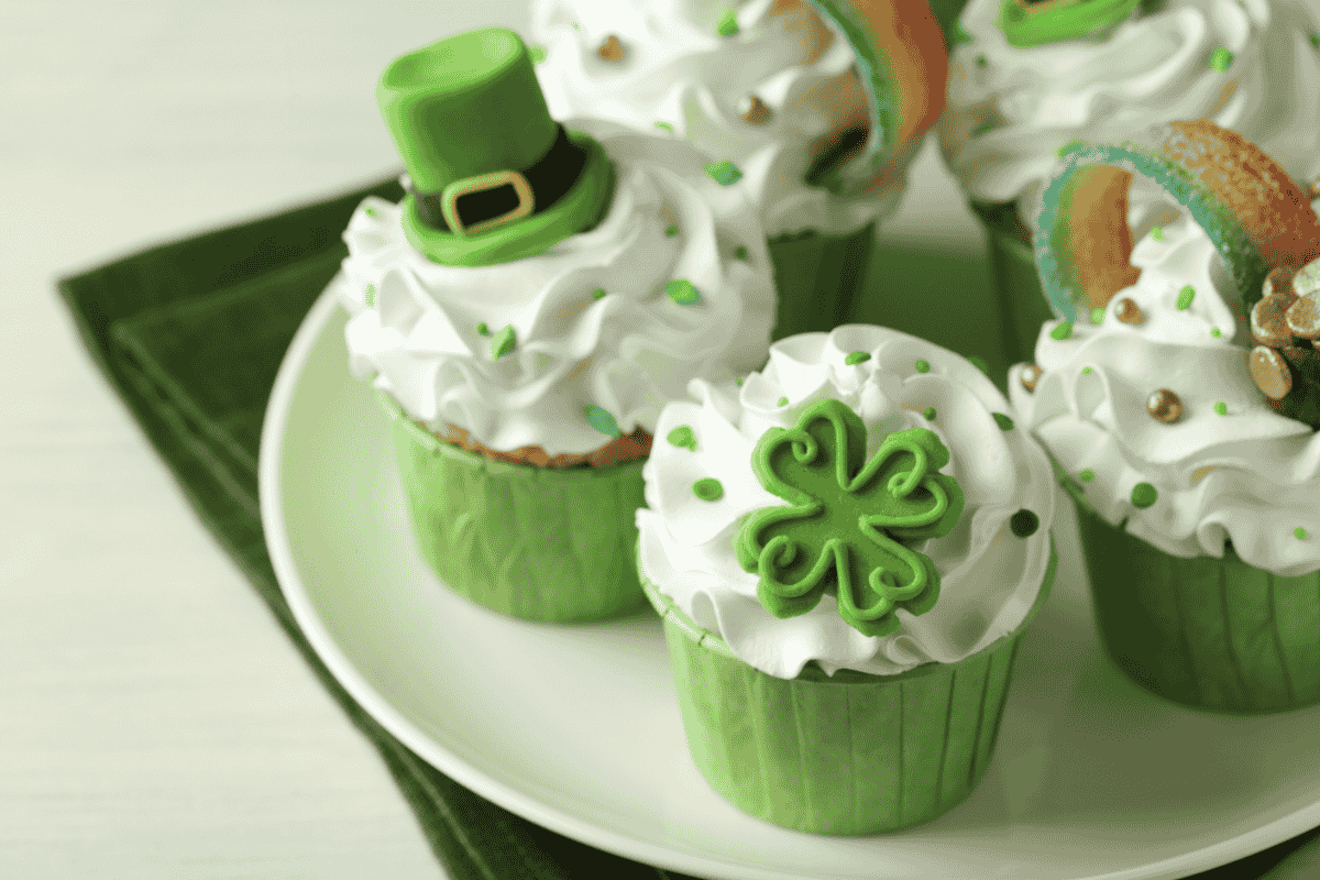 Four St. Patrick’s Day cupcakes with green wrappers and festive decorations on a white plate.