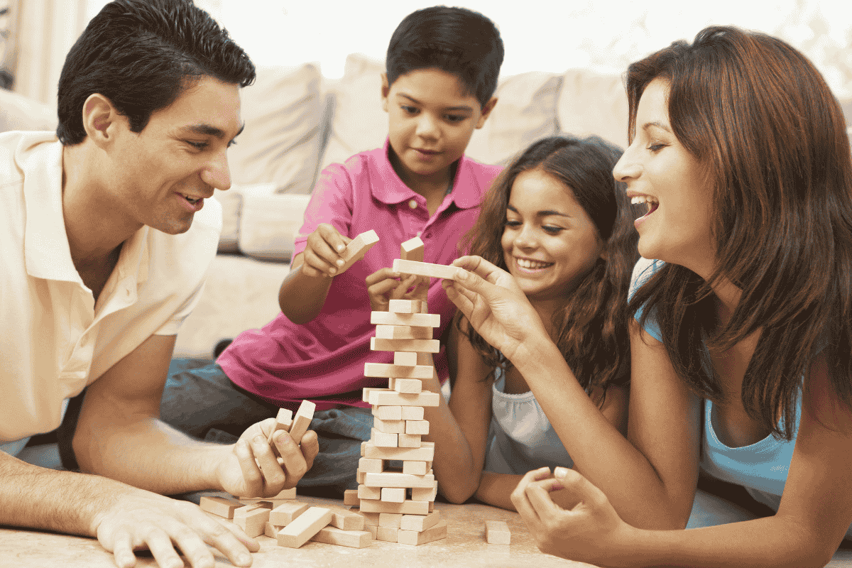 A family of four plays a game of Jenga together, smiling and laughing in a cozy living room.