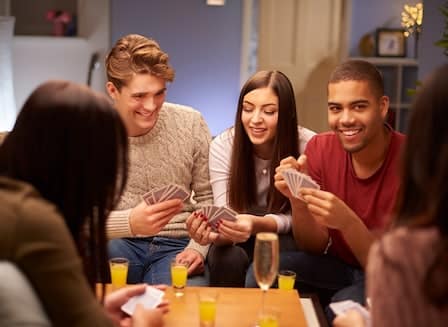 Group of friends enjoying a card game at a cozy gathering, with drinks on the table and a warm atmosphere.