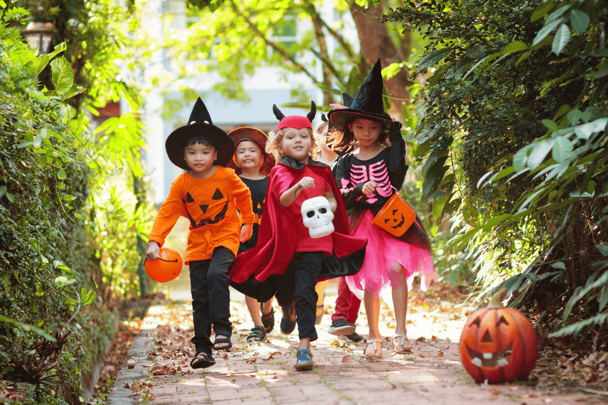 Children in Halloween costumes carrying pumpkin buckets while trick-or-treating outdoors at San Diego RV Resort’s Trunk or Treat event.