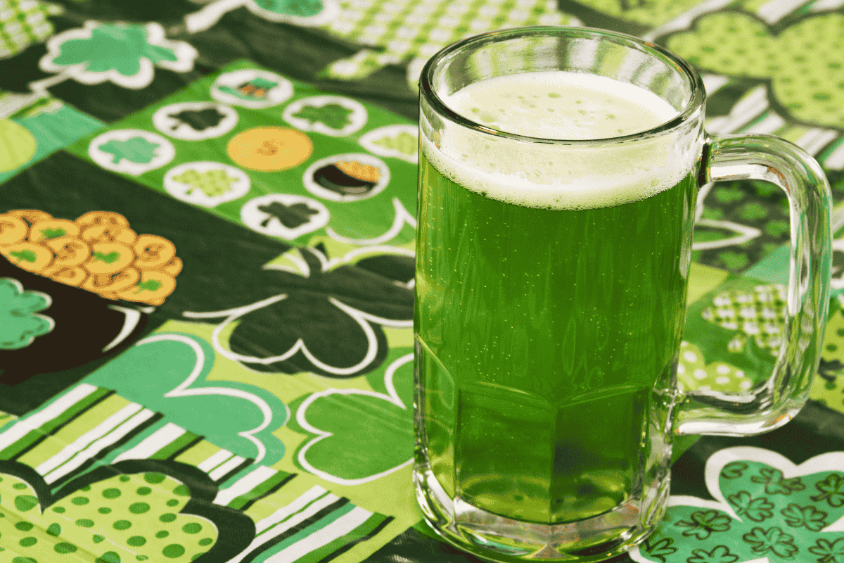 A glass of green beer on a festive green and shamrock-patterned tablecloth, perfect for St. Patrick's Day celebrations.