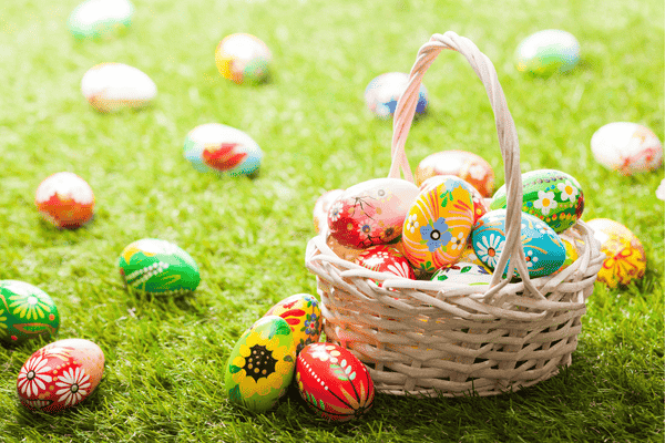 Colorful Easter eggs in a white wicker basket on green grass, surrounded by more decorated eggs, creating a festive spring atmosphere.