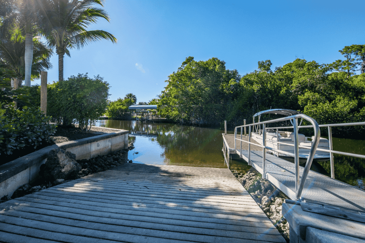 Boat ramp beside a docked white boat, surrounded by lush greenery and palm trees under a blue sky.