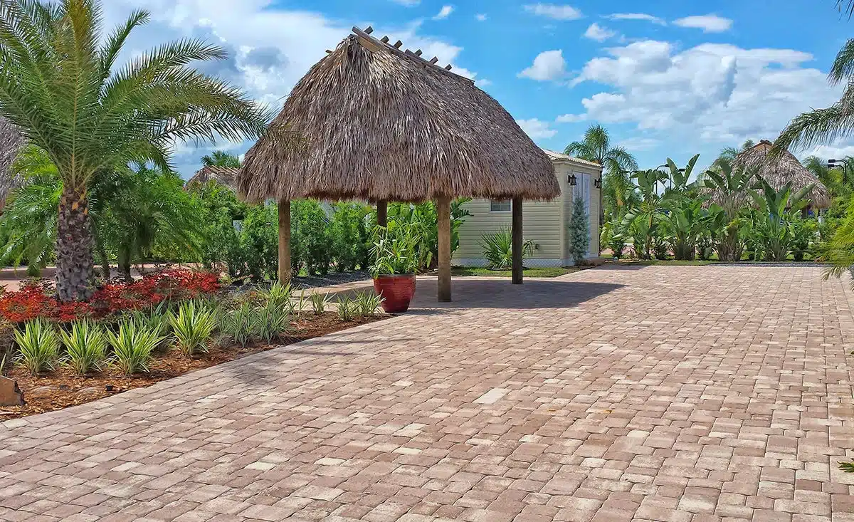 Thatched-roof hut and palm trees beside a paved area under a blue sky with scattered clouds at Silver Palms RV Resort.